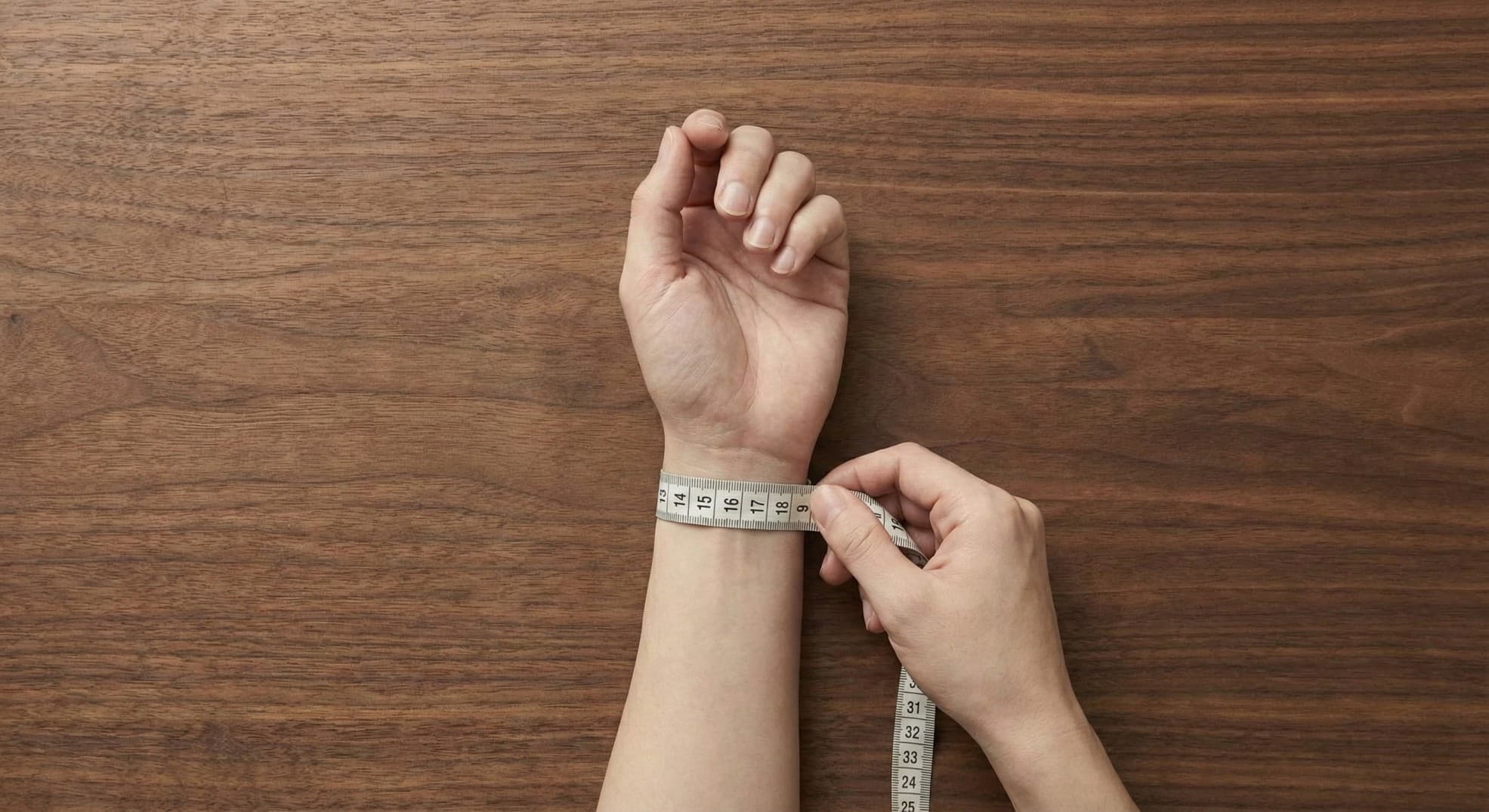 Flexible measuring tape being wrapped around the wrist bone to find the total circumference.